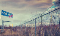 Abandoned property/brownfield site with For Sale sign and barbed wire.