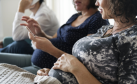 Two pregnant woman having a conversation over a cellphone, sitting sit by side.