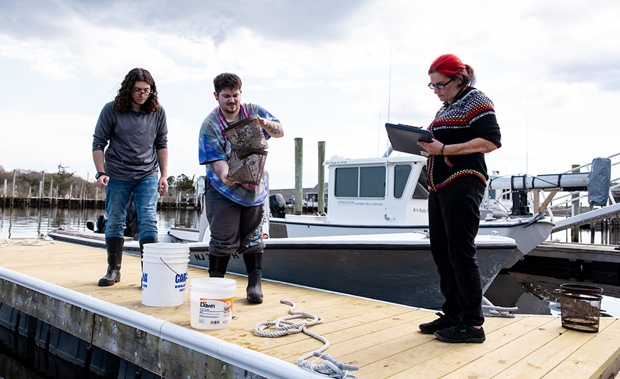 From left: Stockton Marine Science majors Alexander Wroblewski, a senior from Drexel Hill, Pa.; River Hammell, a senior from Wenonah; and Jess Taylor, a senior from Whiting, record fish monitoring data at the dock at Stockton’s Marine Field Station in Port Republic. PROVIDED BY SUSAN ALLEN/STOCKTON UNIVERSITY